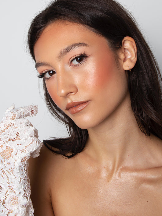 Woman with long dark hair, glowing makeup, and a white lace glove, posing against a plain background.