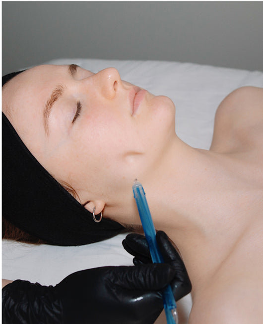 Person lying down receiving a cosmetic injection in the jawline by a gloved professional.