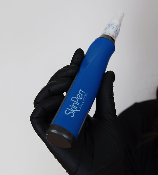 A hand in a black glove holds a blue SkinPen Precision microneedling device against a plain background.