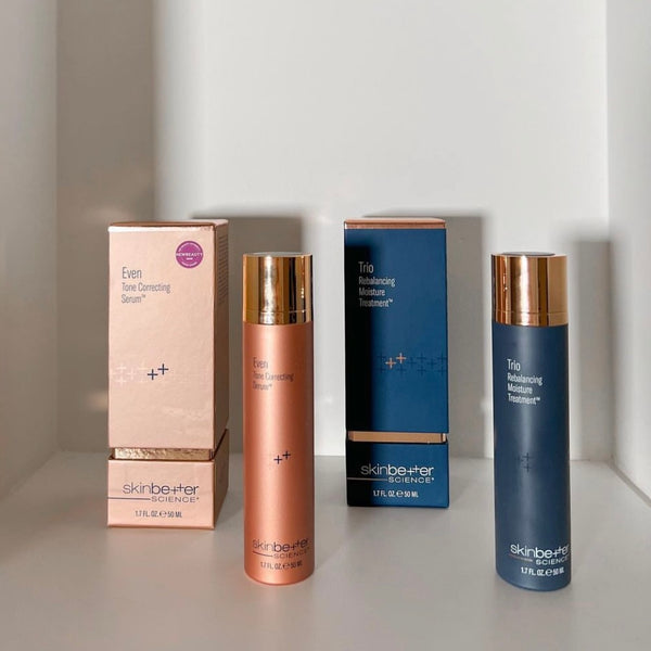 Two skinbetter science skincare products with their boxes, one rose gold and one navy blue, placed on a white shelf.