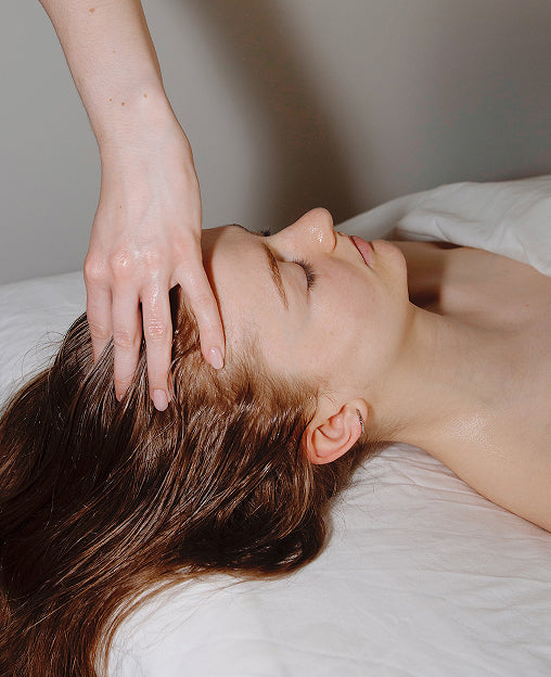 A woman receives a relaxing head massage while lying on a white massage table.