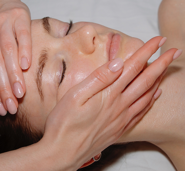 Woman with closed eyes receiving a gentle facial massage with clean, well-manicured hands on her face.