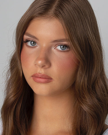 A young woman with long brown hair and blue eyes looks seriously at the camera against a plain background.